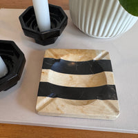 Marble coaster with black stripes on a table with candles and a vase.