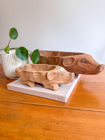 Two wooden pig-shaped planters on a wooden surface with a white background